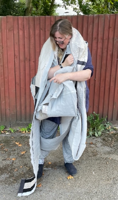 A laughing woman is wrapped in a long piece of quilting.