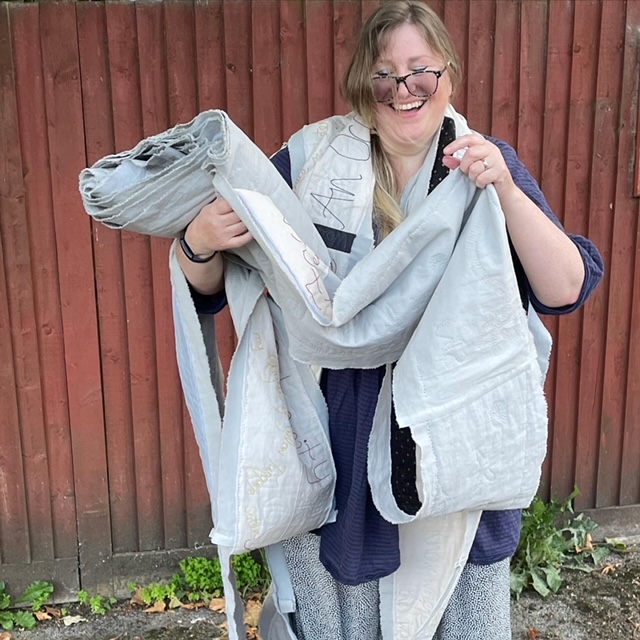 A laughing woman wrapped in a long strip of quilting.