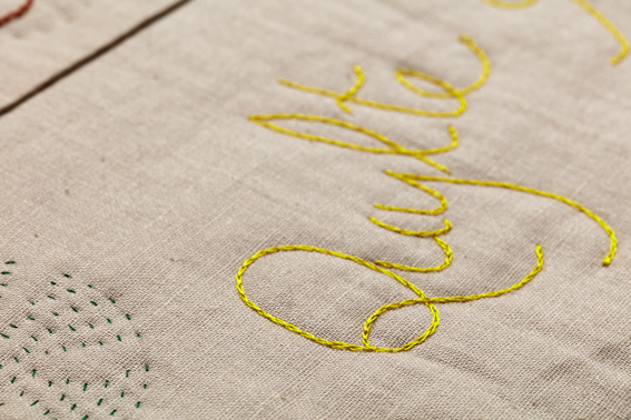 The word 'Quylte' embroidered in yellow thread on to cream fabric