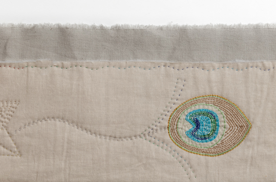 An embroidered and quilted peacock feather on cream fabric