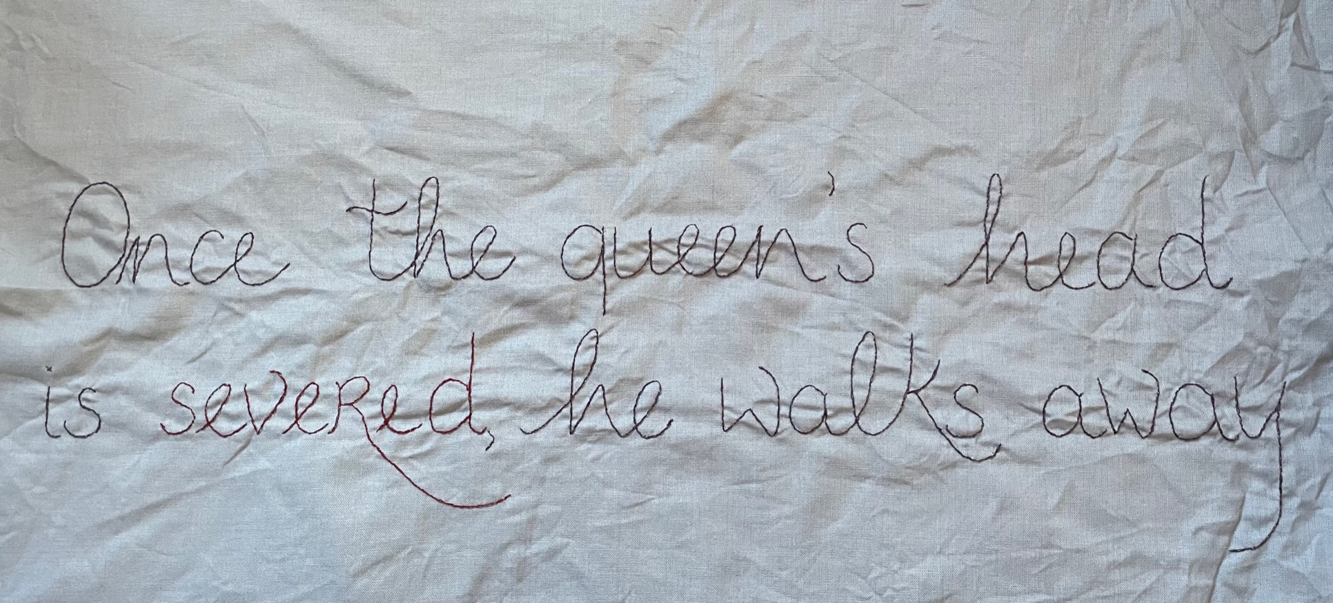 White fabric embroidered with the words 'Once the queen's head is severed, he walks away'