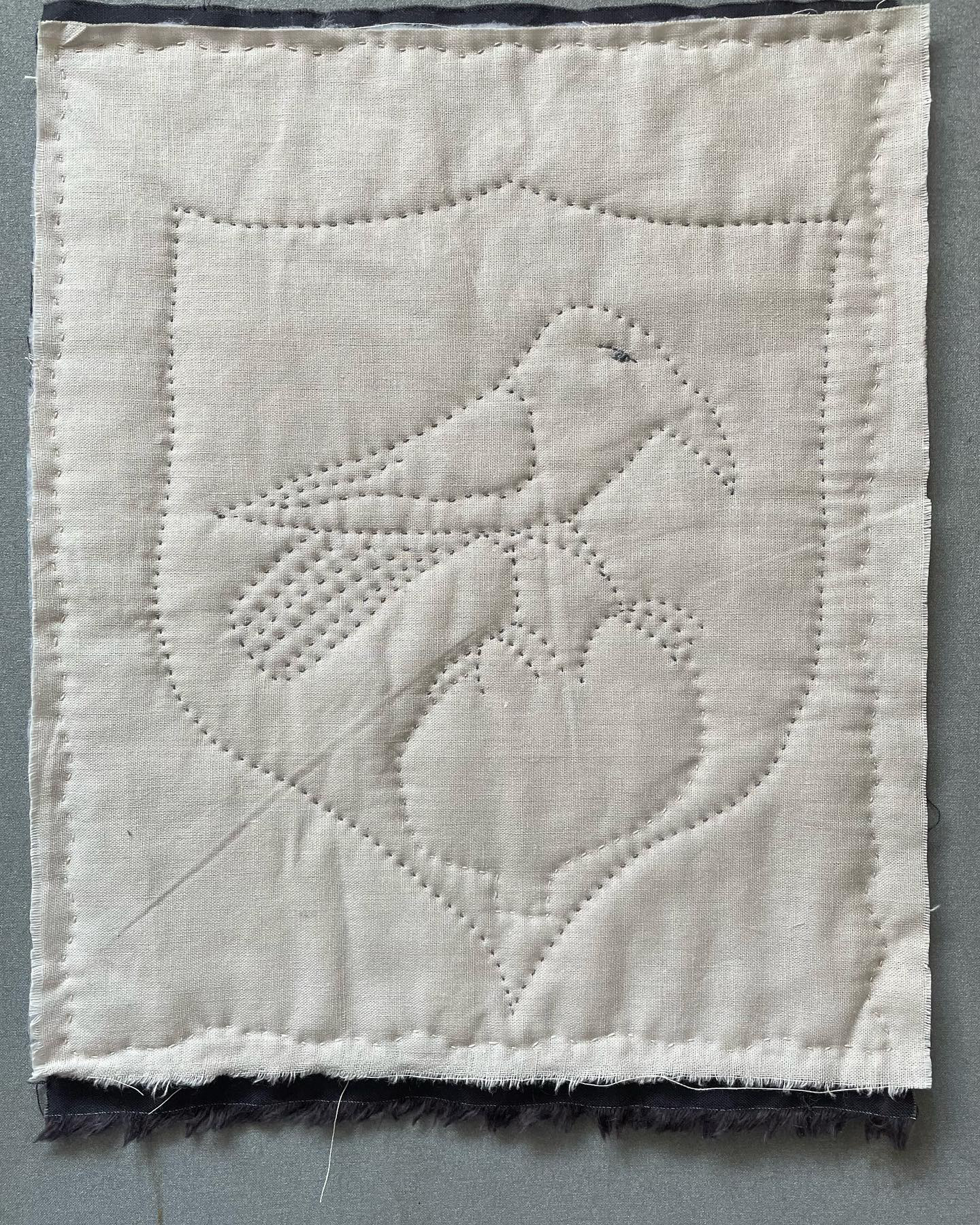 Quilted grey fabric depicting a bird presented within a shield shape