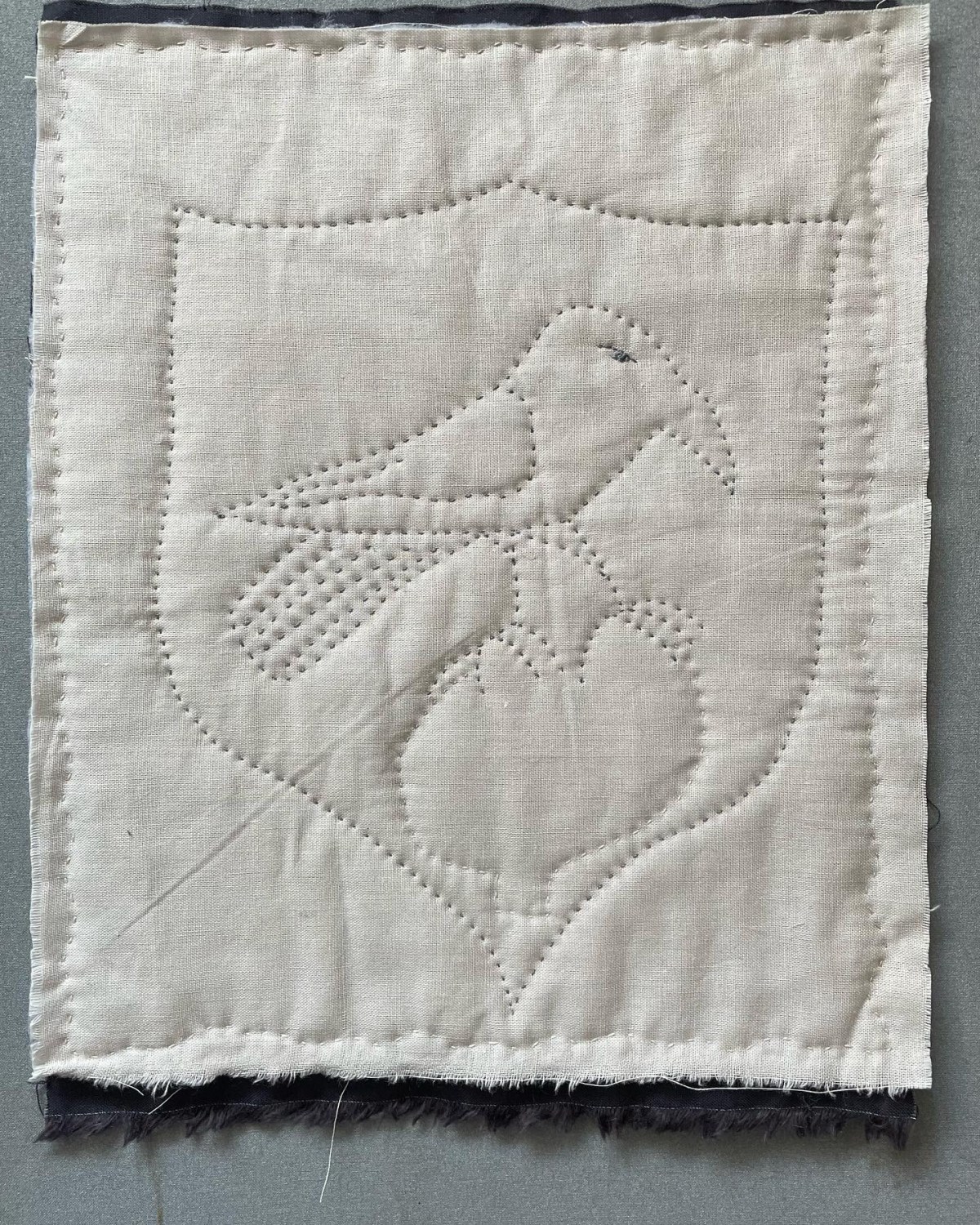Quilted grey fabric depicting a bird presented within a shield shape
