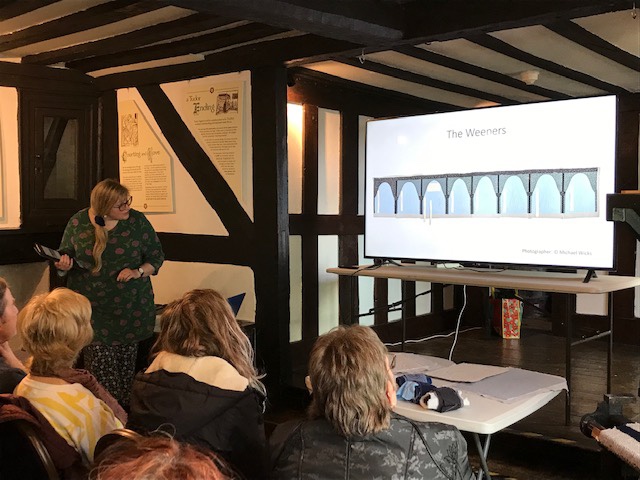 A woman bends to look round at a screen, showing a piece of textile art work described on screen as The Weepers.